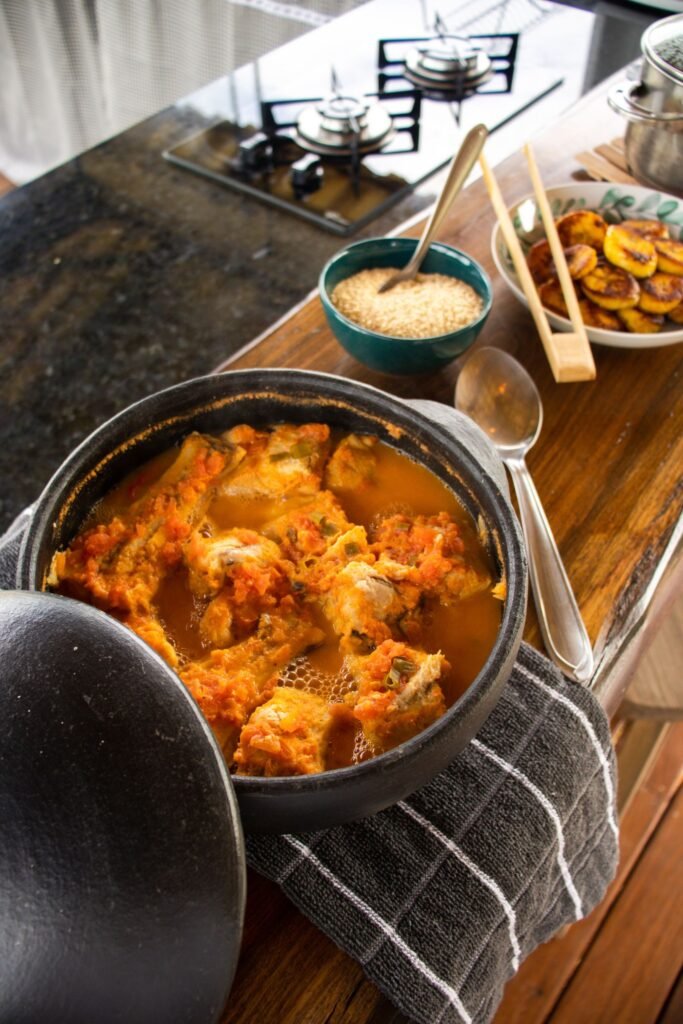 Moqueca brasileira servida em panela de barro sobre a mesa, acompanhada de arroz e banana-da-terra