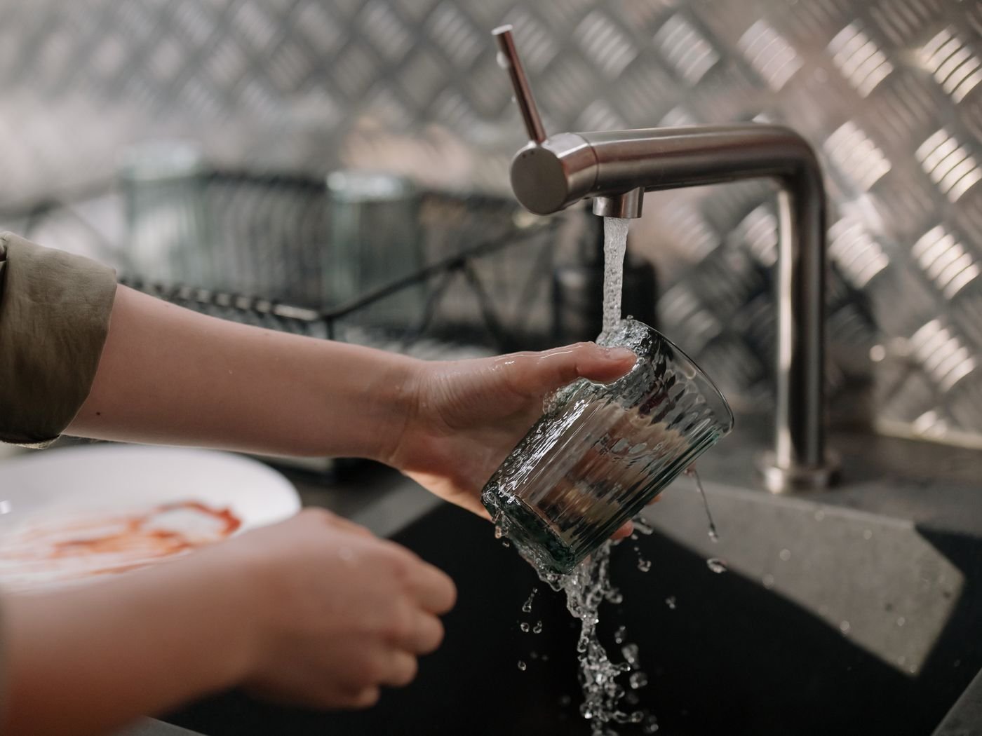 Mãos lavando um copo sob água corrente da torneira