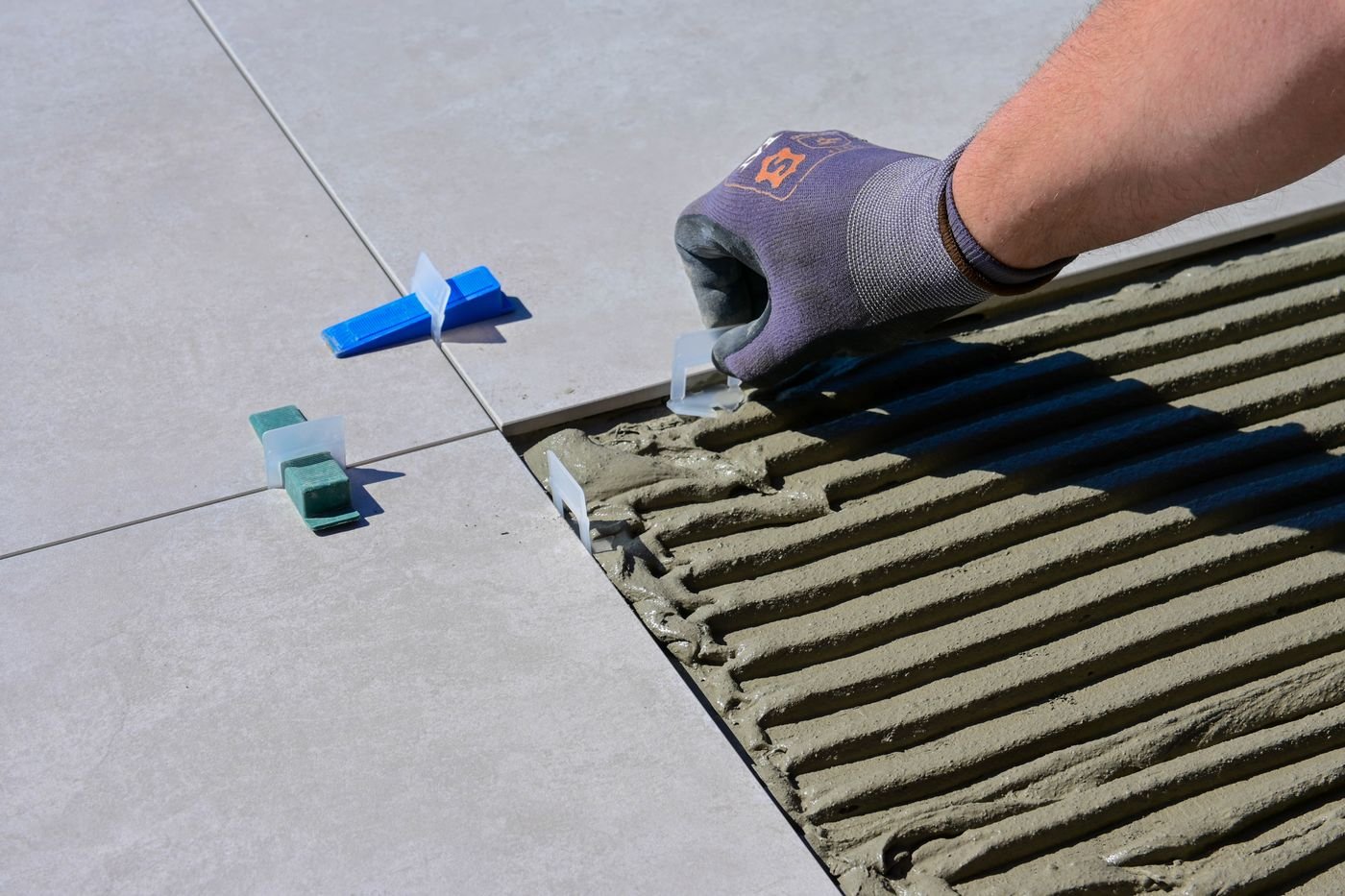 Mão com luva alinhando porcelanato de grande formato com niveladores sobre argamassa
