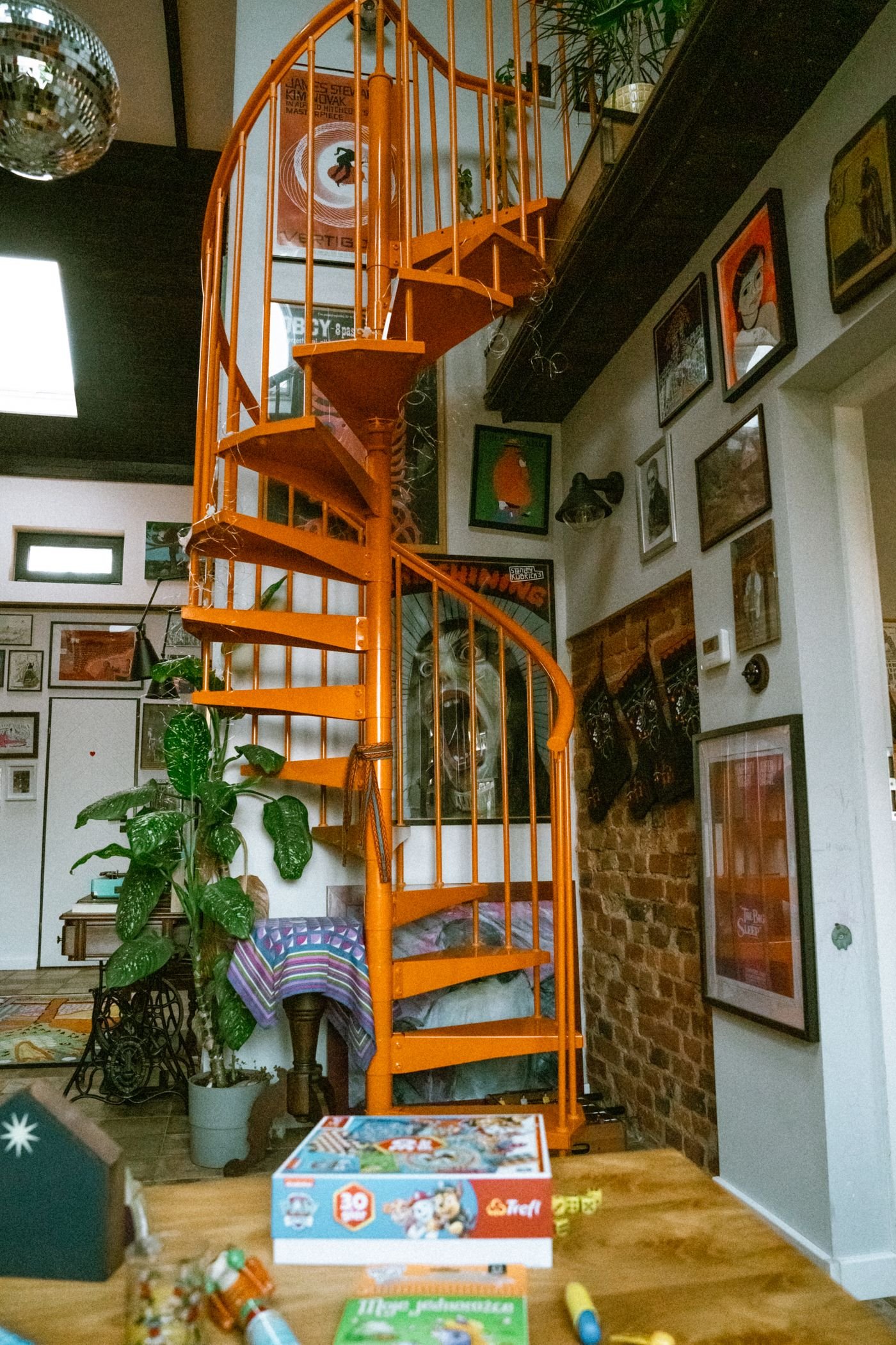 Escada caracol laranja num ambiente cheio de quadros e plantas