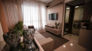 Sala pequena integrada com sofá, painel de TV e cortina clara