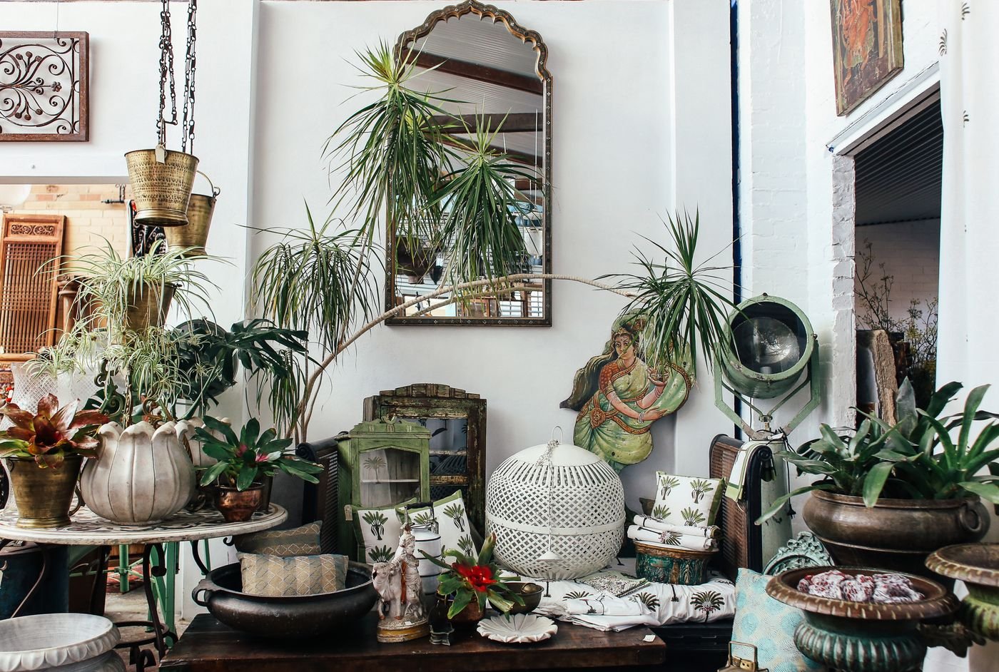 Sala no estilo eclético com plantas, móveis antigos e objetos variados