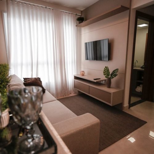 Sala pequena integrada com sofá, painel de TV e cortina clara